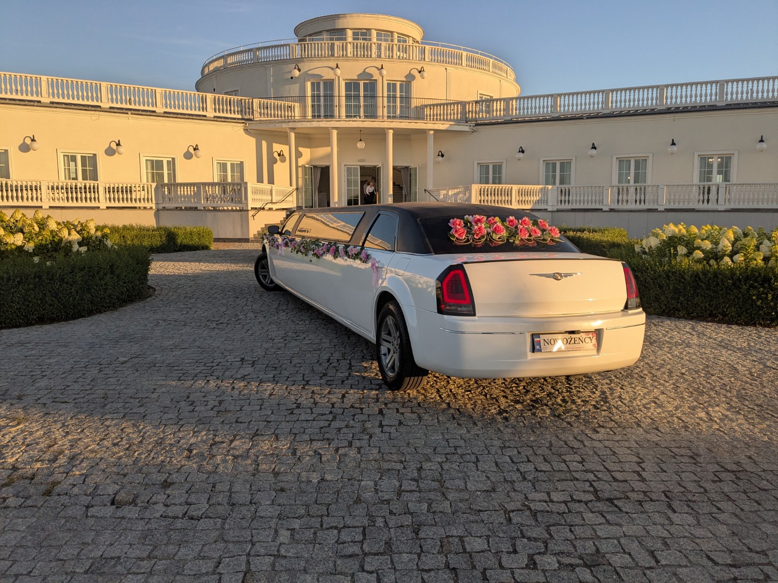 Tył limuzyny Chrysler z tablicą NOWOŻEŃCY przed salą weselną