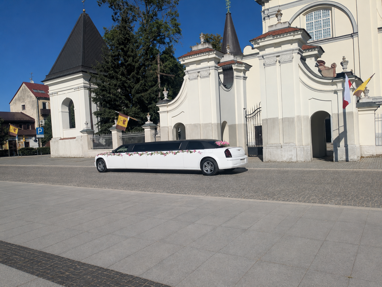 Biała limuzyna Chrysler zaparkowana na placu przed zabytkowym kościołem