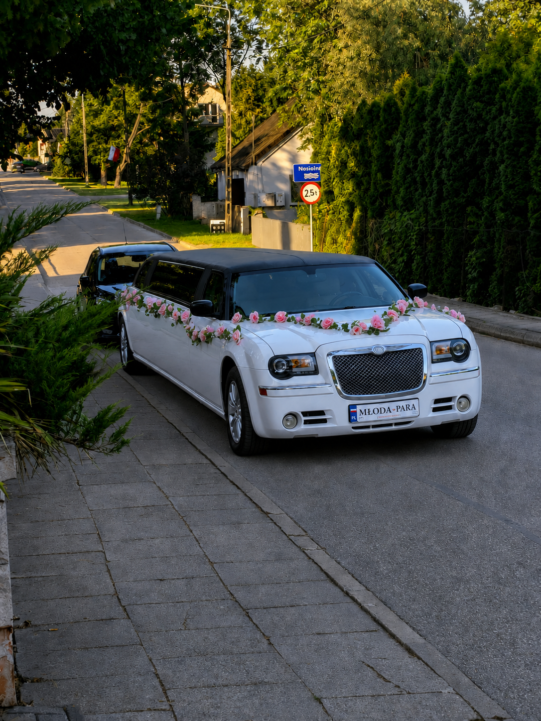 Biała limuzyna Chrysler z tablicą MŁODA-PARA na podjazdowej ulicy