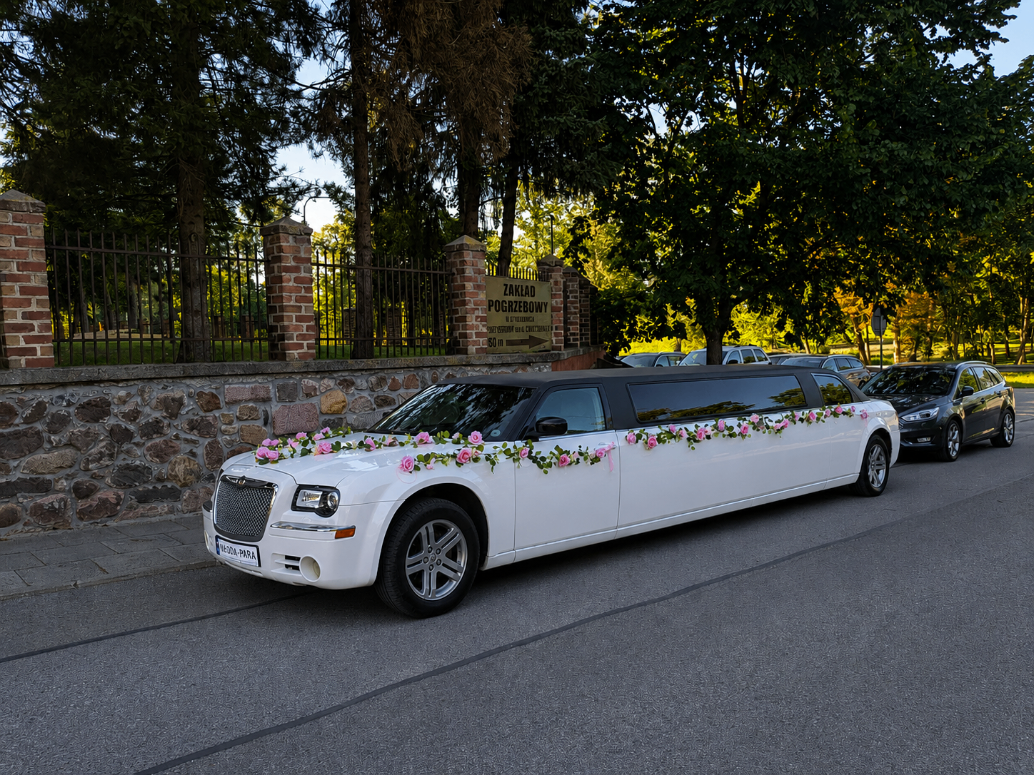 Udekorowana limuzyna Chrysler z tablicą MŁODA-PARA przy kamiennym murze
