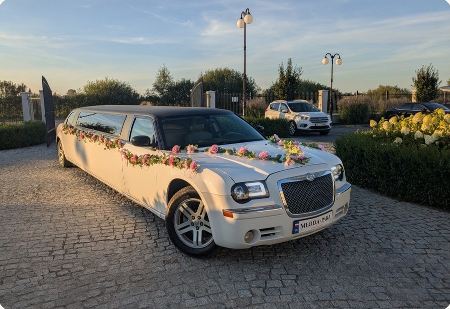 Biała limuzyna Chrysler udekorowana różami na brukowanym podjeździe