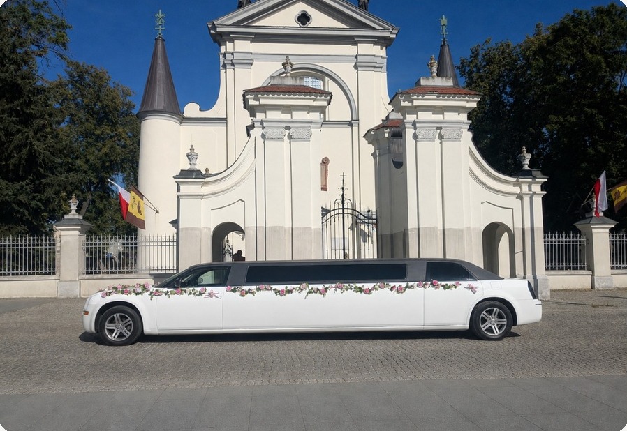 Biała limuzyna Chrysler zaparkowana przed zabytkową bramą kościoła