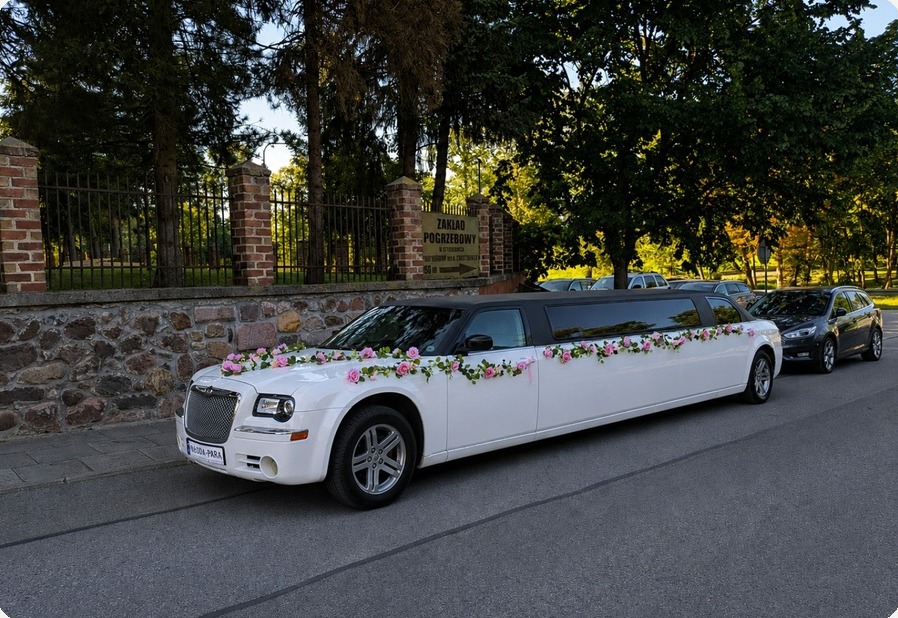 Limuzyna Chrysler udekorowana kwiatami zaparkowana przy kamiennym murze