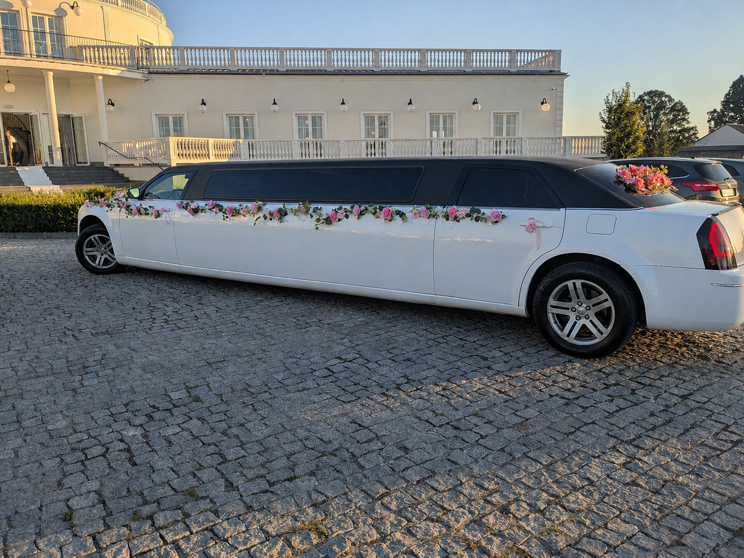 Limuzyna Chrysler z girlandą różowych róż przed białym pałacem weselnym